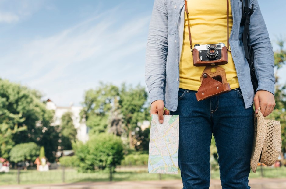 Midsection of tourist man carrying camera and holding map and hat at park