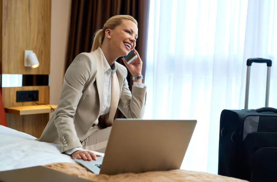 Happy businesswoman sitting on the bed in hotel room and talking on mobile phone