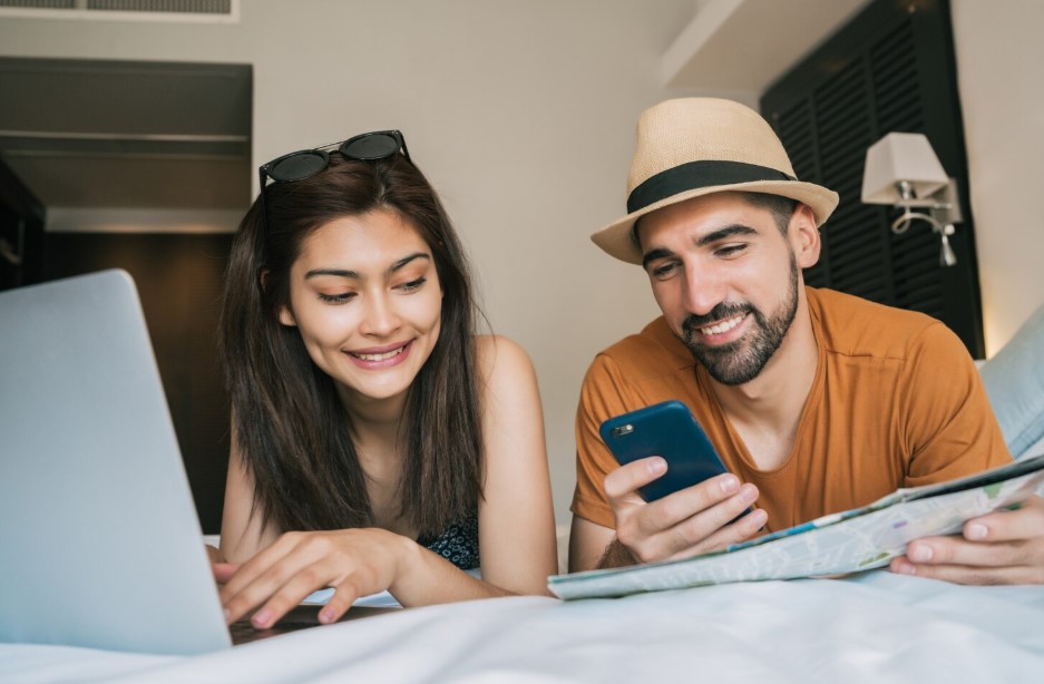 Portrait of lovely couple organizing their trip with laptop and mobile phone at the hotel room
