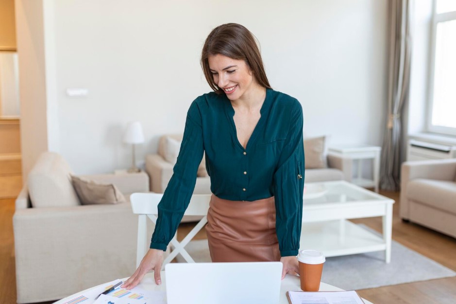 Smiling young female employee stand at desk in office look in distance thinking or visualizing career success happy businesswoman plan or dream at workplace business vision concept