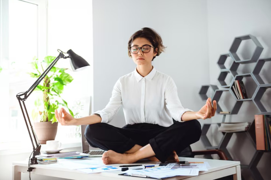 Young beautiful businesswoman meditating on table at workplace in office.