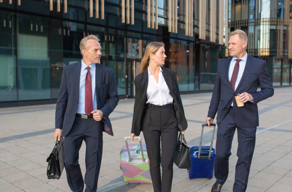 Confident businesspeople travelling with luggage, walking to hotel, wheeling suitcases, talking. Front view. Business trip or corporate communication concept