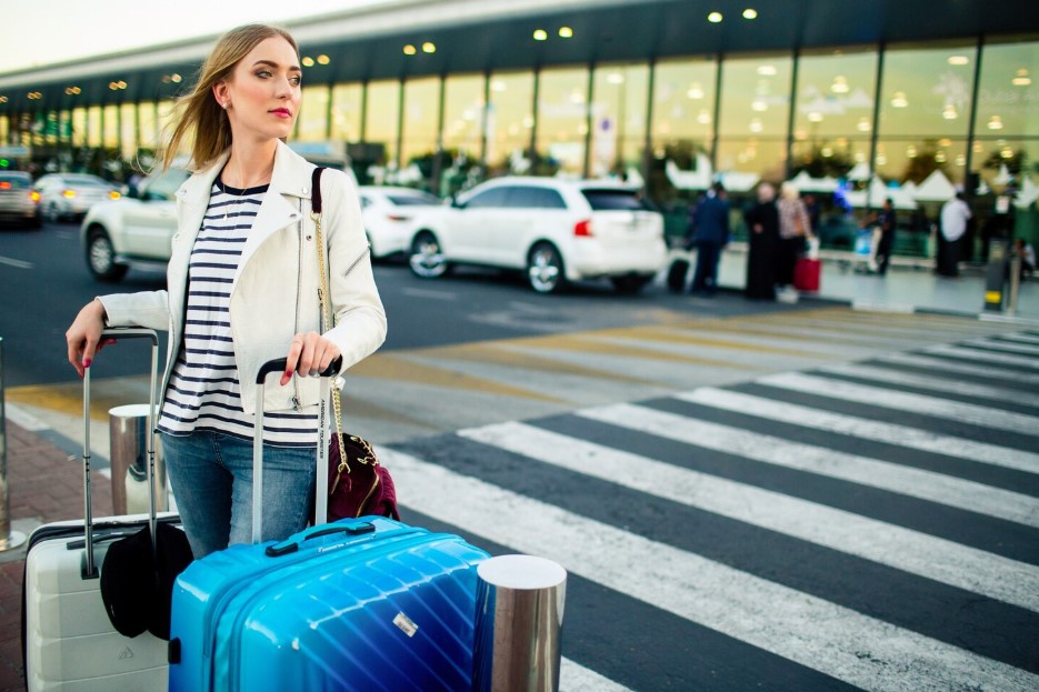 Stunning blonde lady with blue and white suitcases stands before crossing on the street